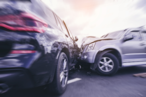 Two cars collide creating an accident. One car is dark in color, the other is silver.