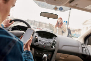 A man stares at his cellphone while driving. He is going to strike a pedestrian!